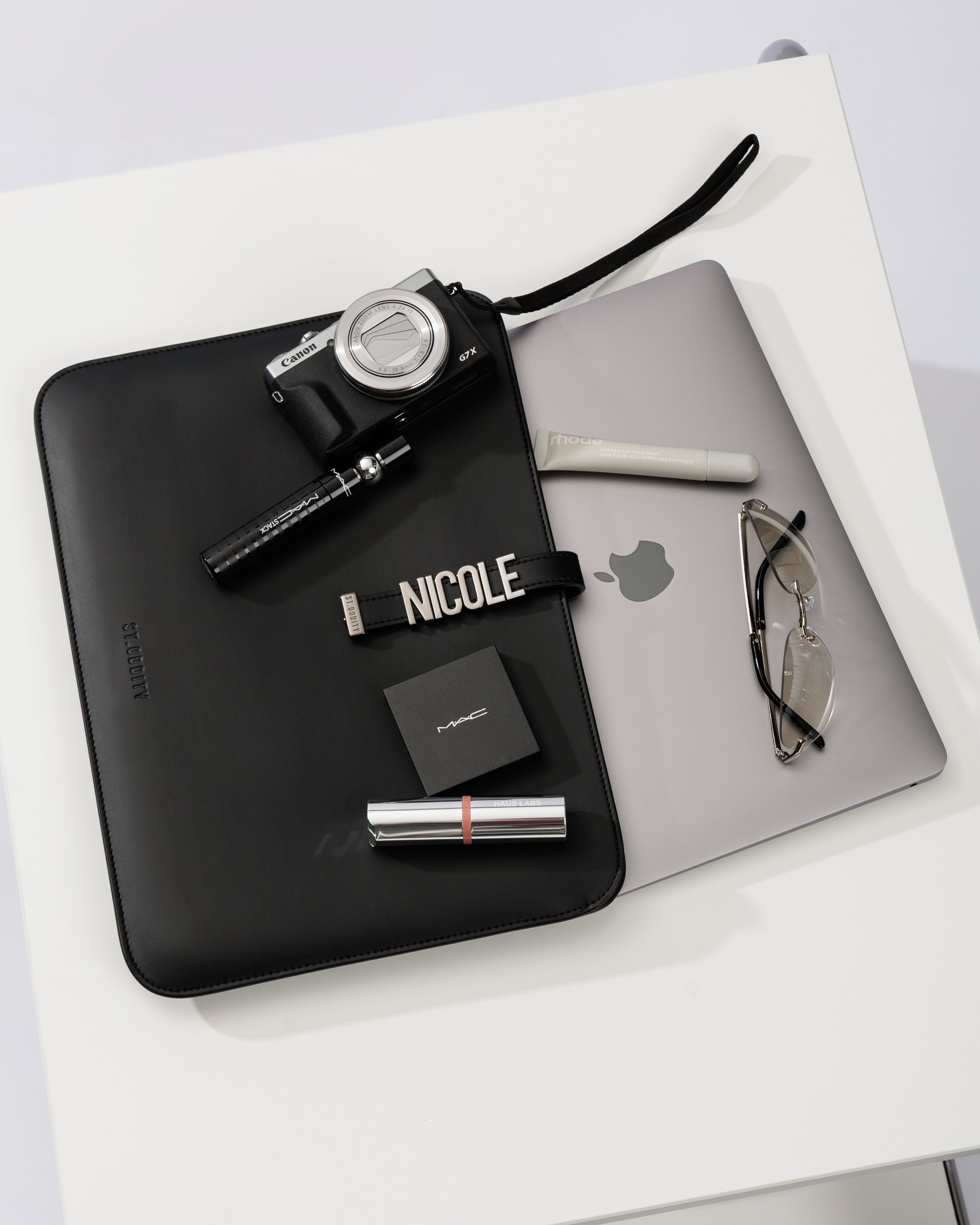 Black laptop sleeve with 'NICOLE' personalisation on a white surface with a laptop and other items.