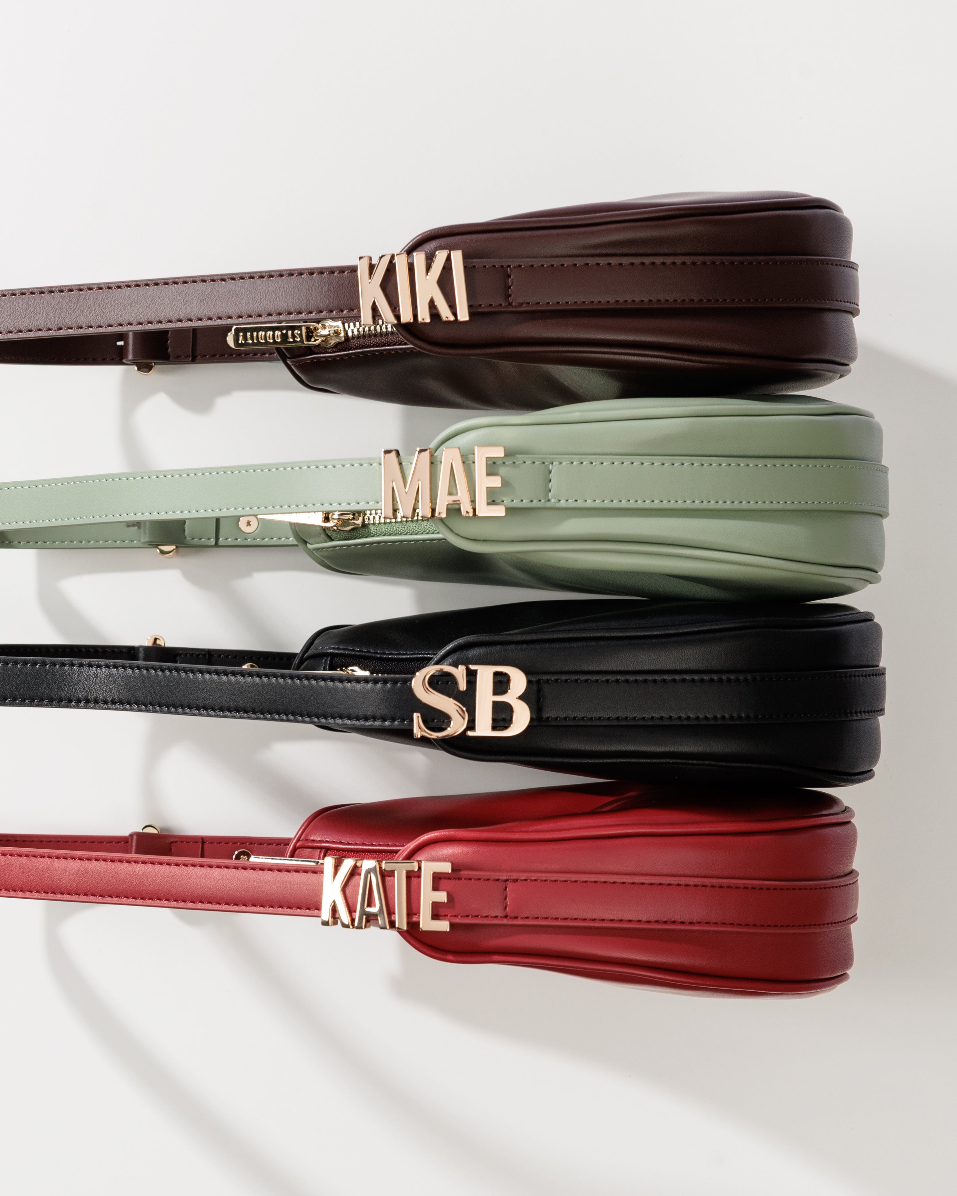 Four Crescent Shoulder Bags in Brown, Sage, Black and Red with gold lettering on a white background.