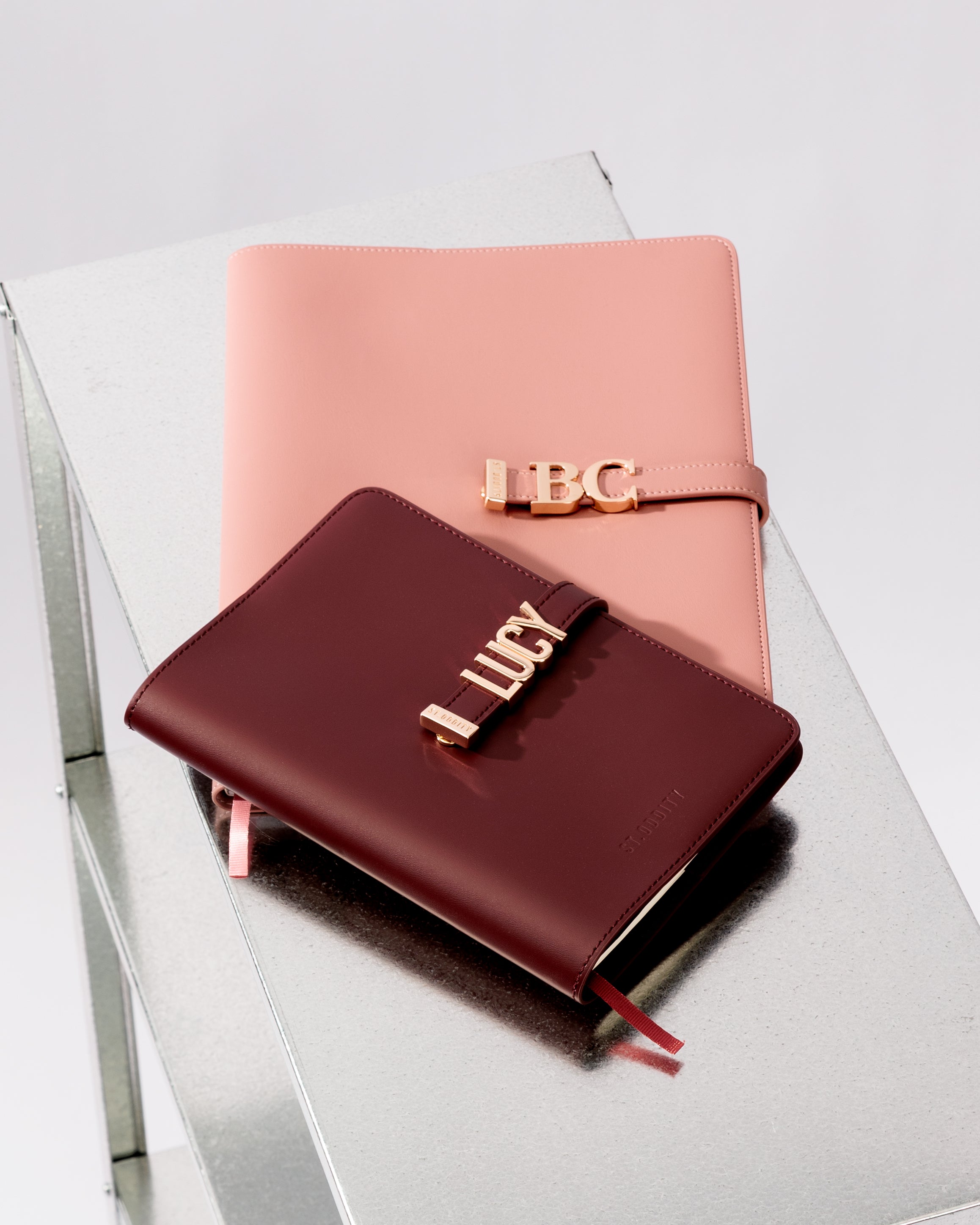 A5 Oxblood and A4 Blush personalised notebooks on a steel table.