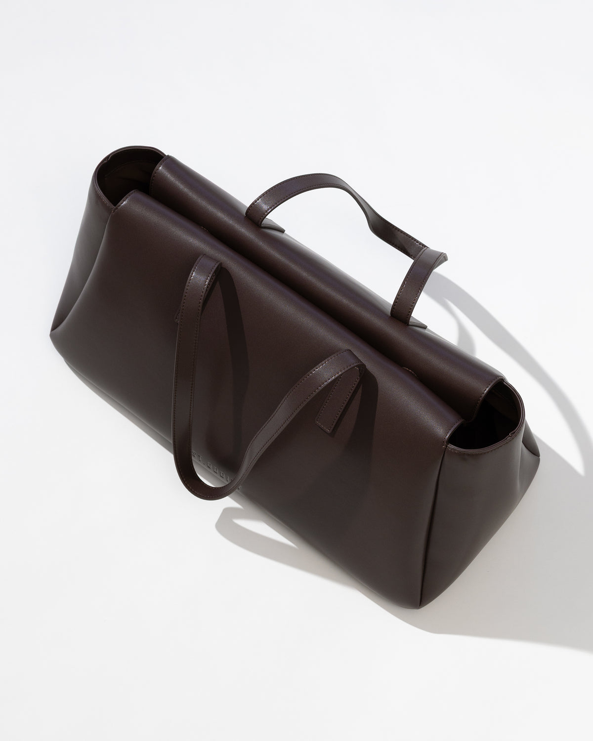 A dark brown leather handbag with dual top handles, photographed from an elevated angle on a clean white background with a soft shadow.