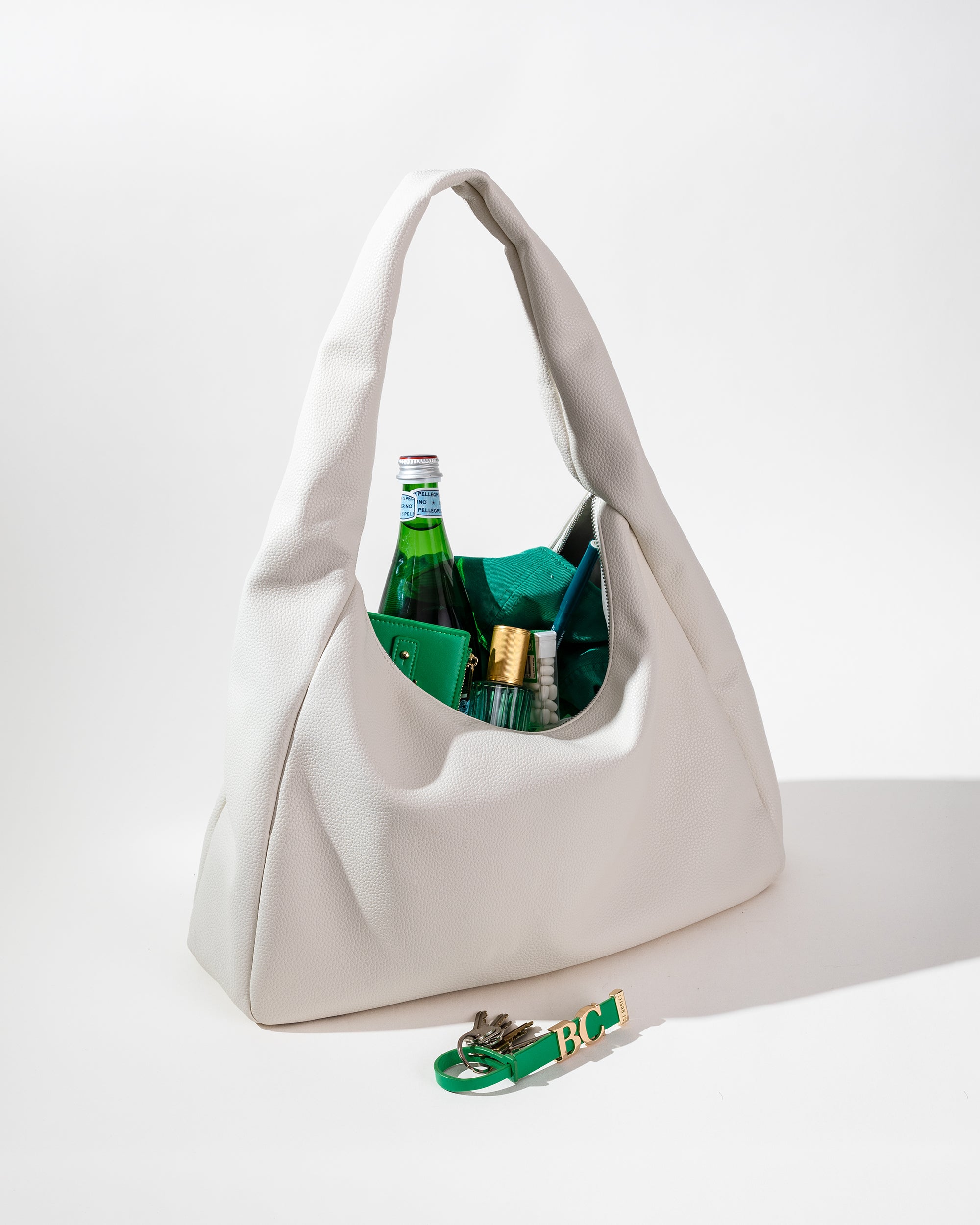 An off white hobo bag with a pebble texture on white, open with green accessories inside.