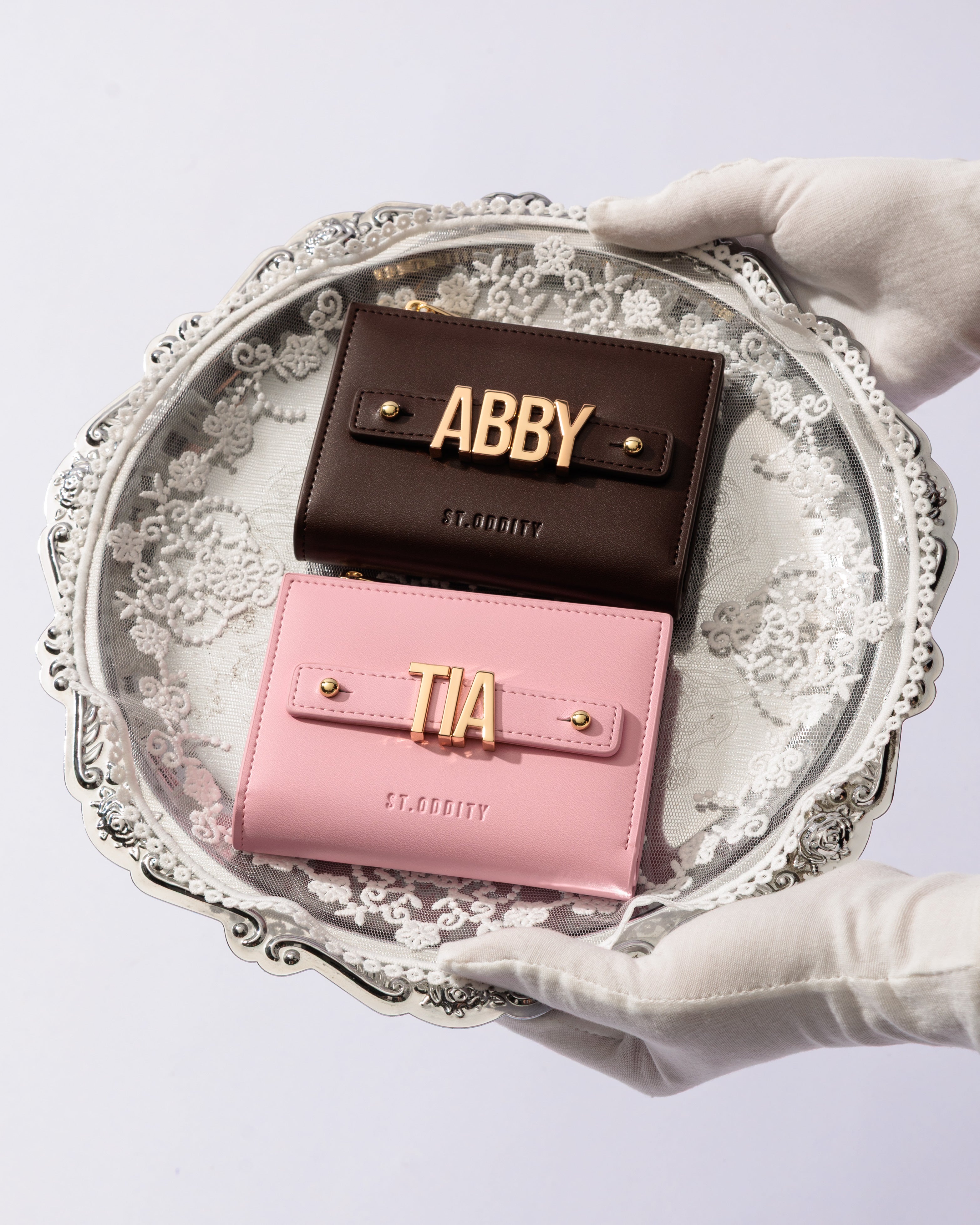 Two wallets, one brown and one pink, with 'ABBY' and 'TIA' personalisation, held on a decorative tray.