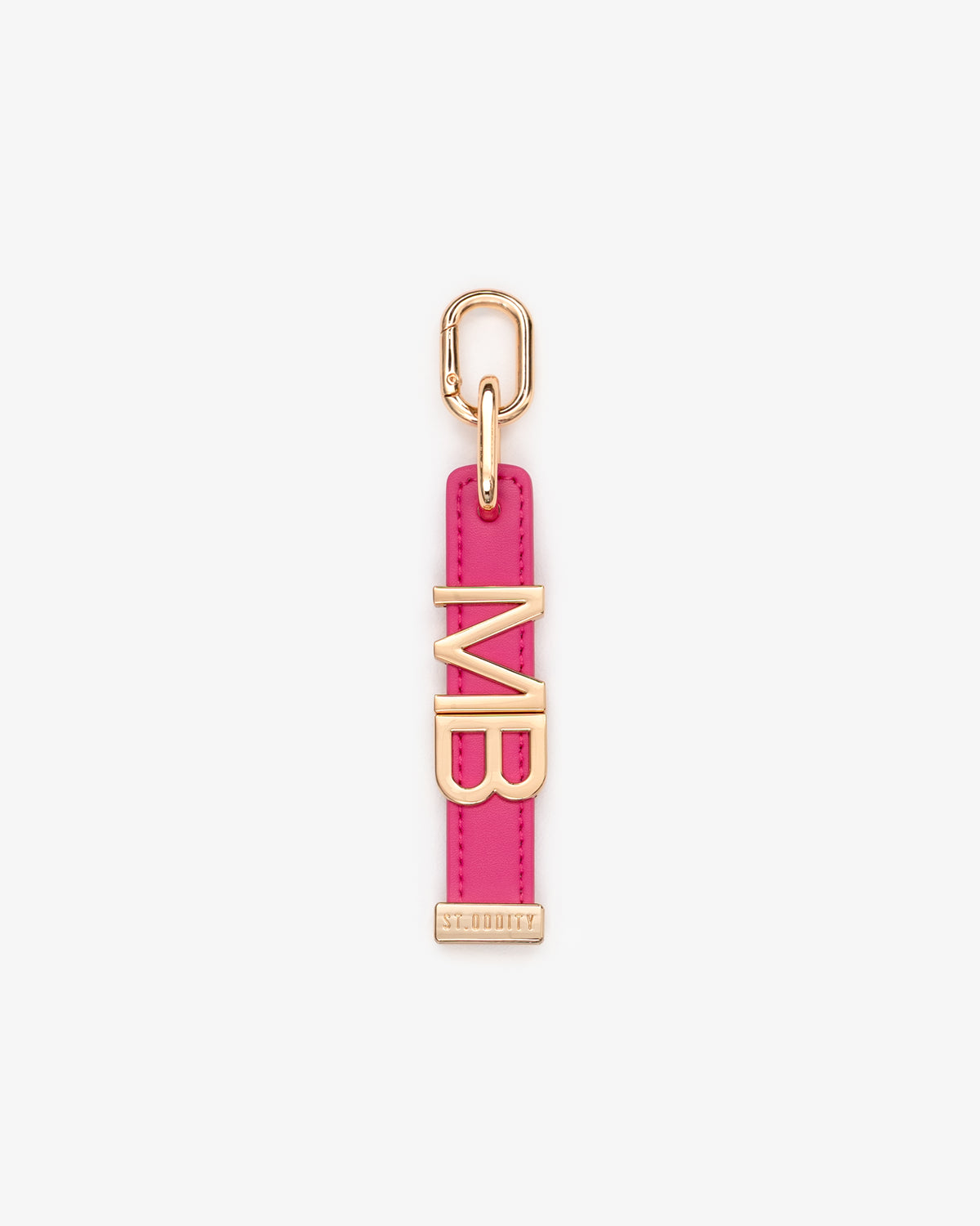 A pink charm featuring gold-tone metal hardware, including a top loop, a vertical strap, and large initials.