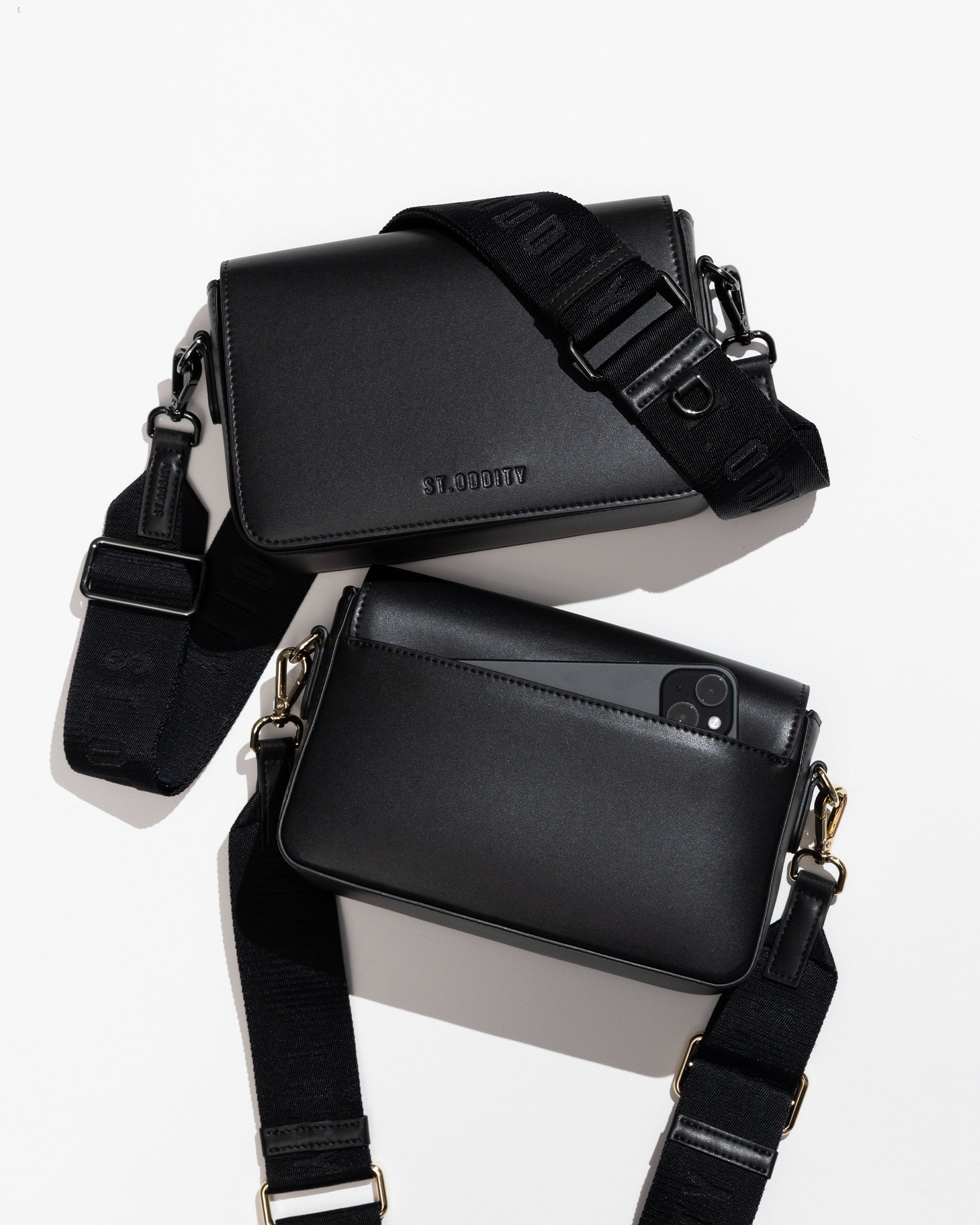 Flatlay of two black crossbody bags with adjustable straps on a white background