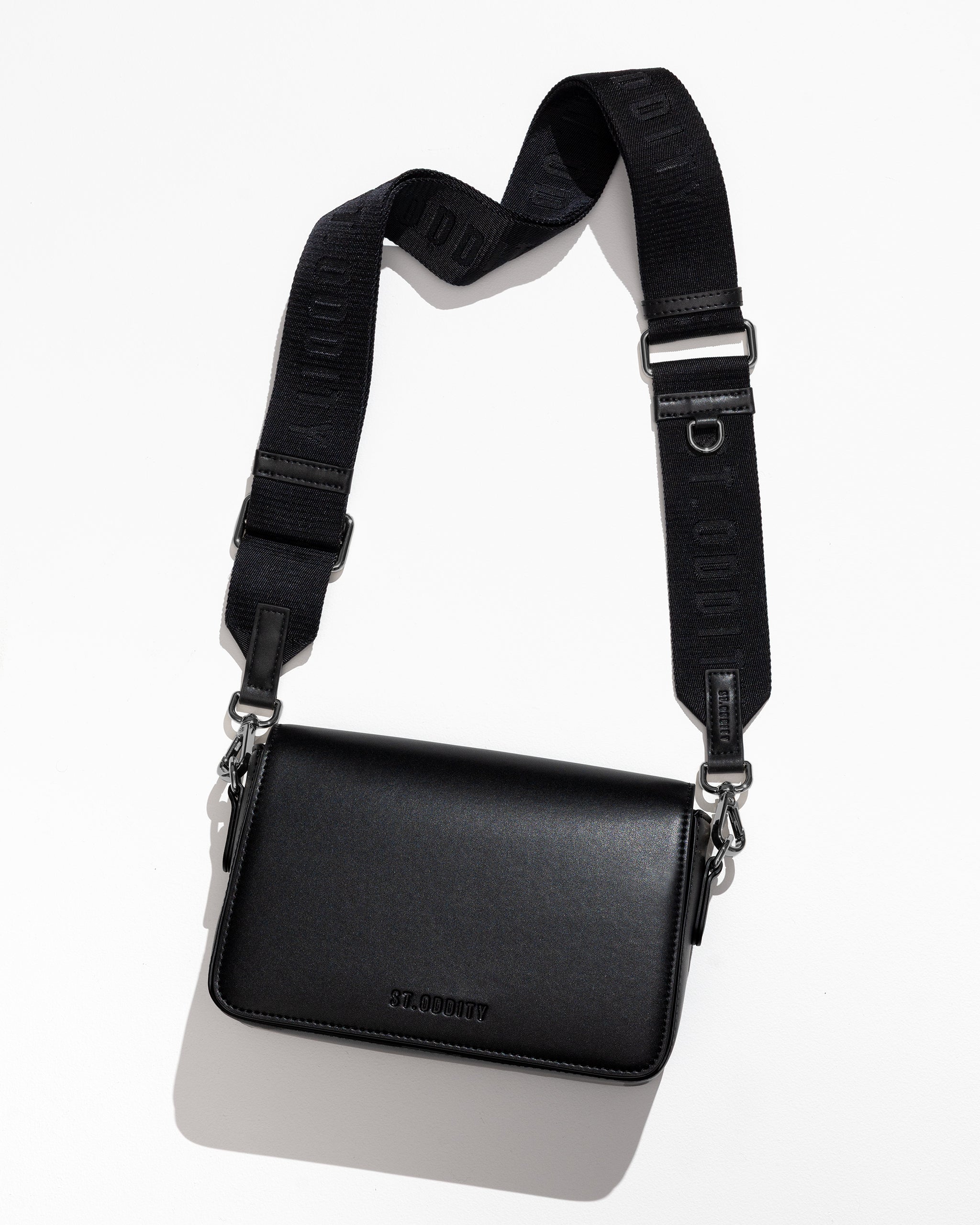 Flatlay of black crossbody bag with adjustable strap on a white background