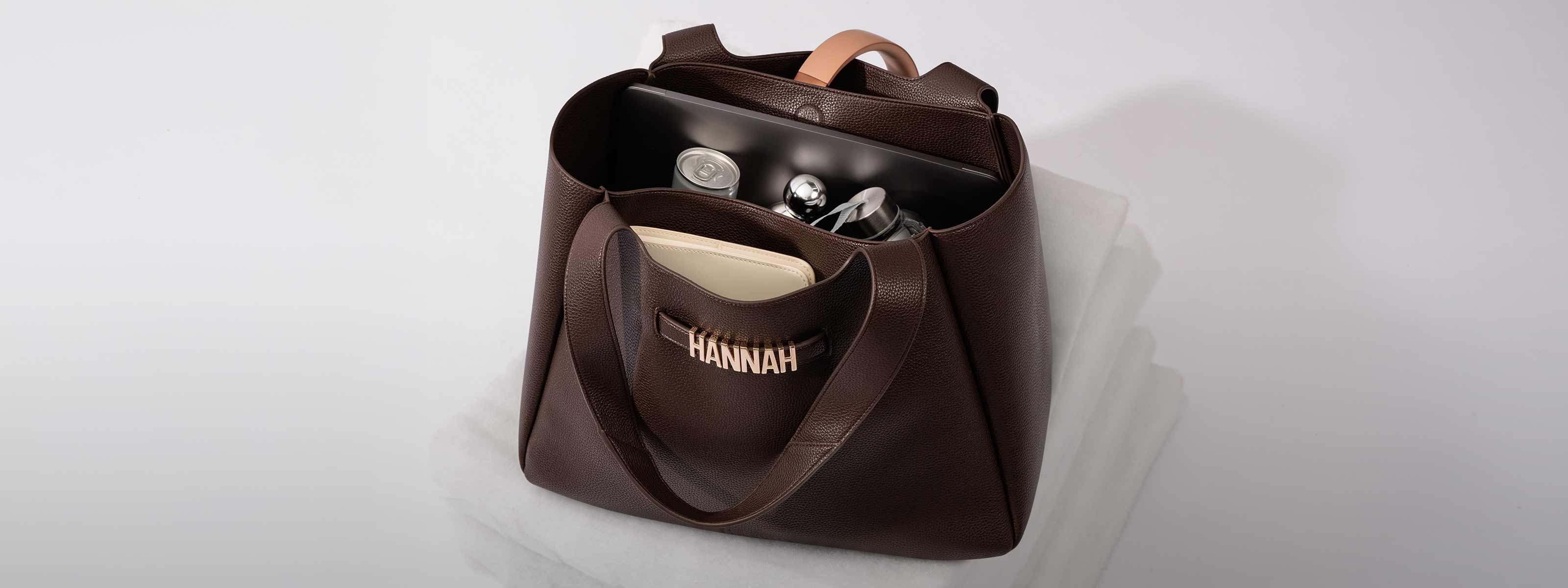 Brown XL Casual TOTE with 'HANNAH' personalisation on a light gray background. Inside there is a laptop, can of drink, water bottle, perfume and A5 notebook.