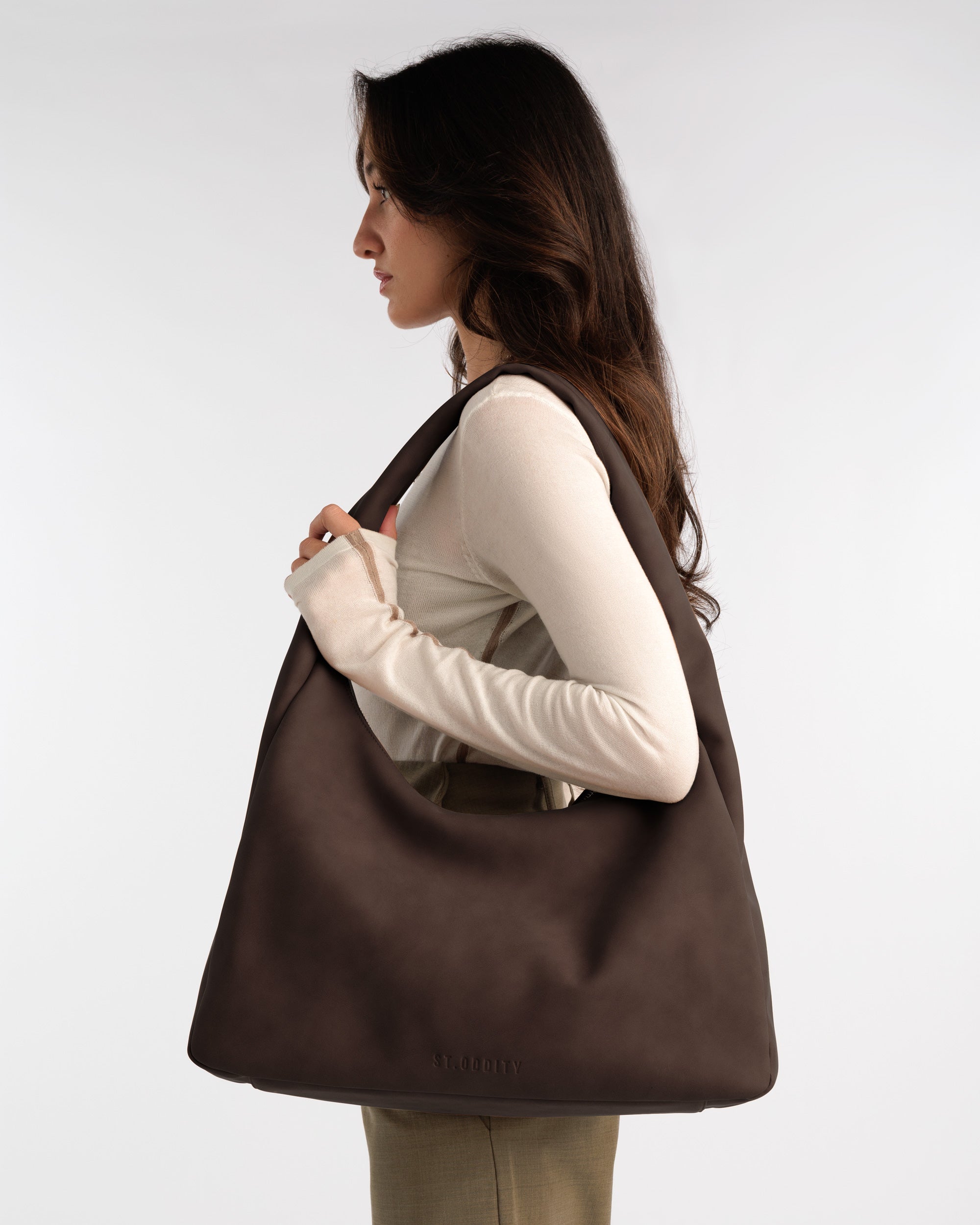 Model holding a chocolate brown faux suede hobo bag with a plain background