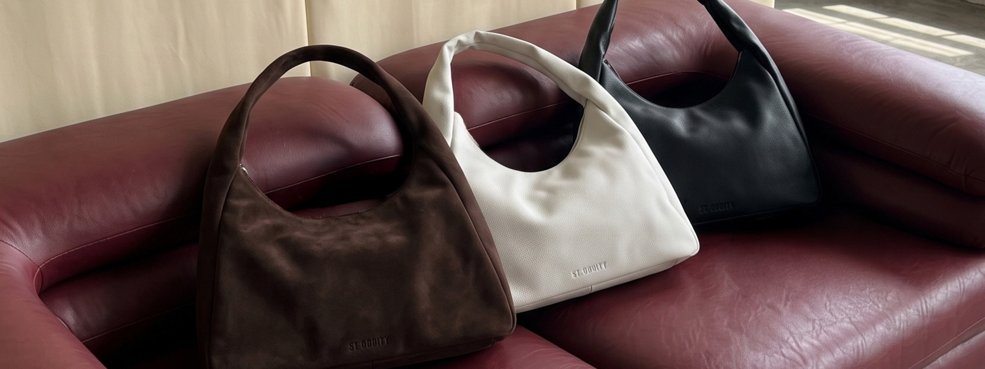 Three handbags in brown, white, and black on a leather couch.