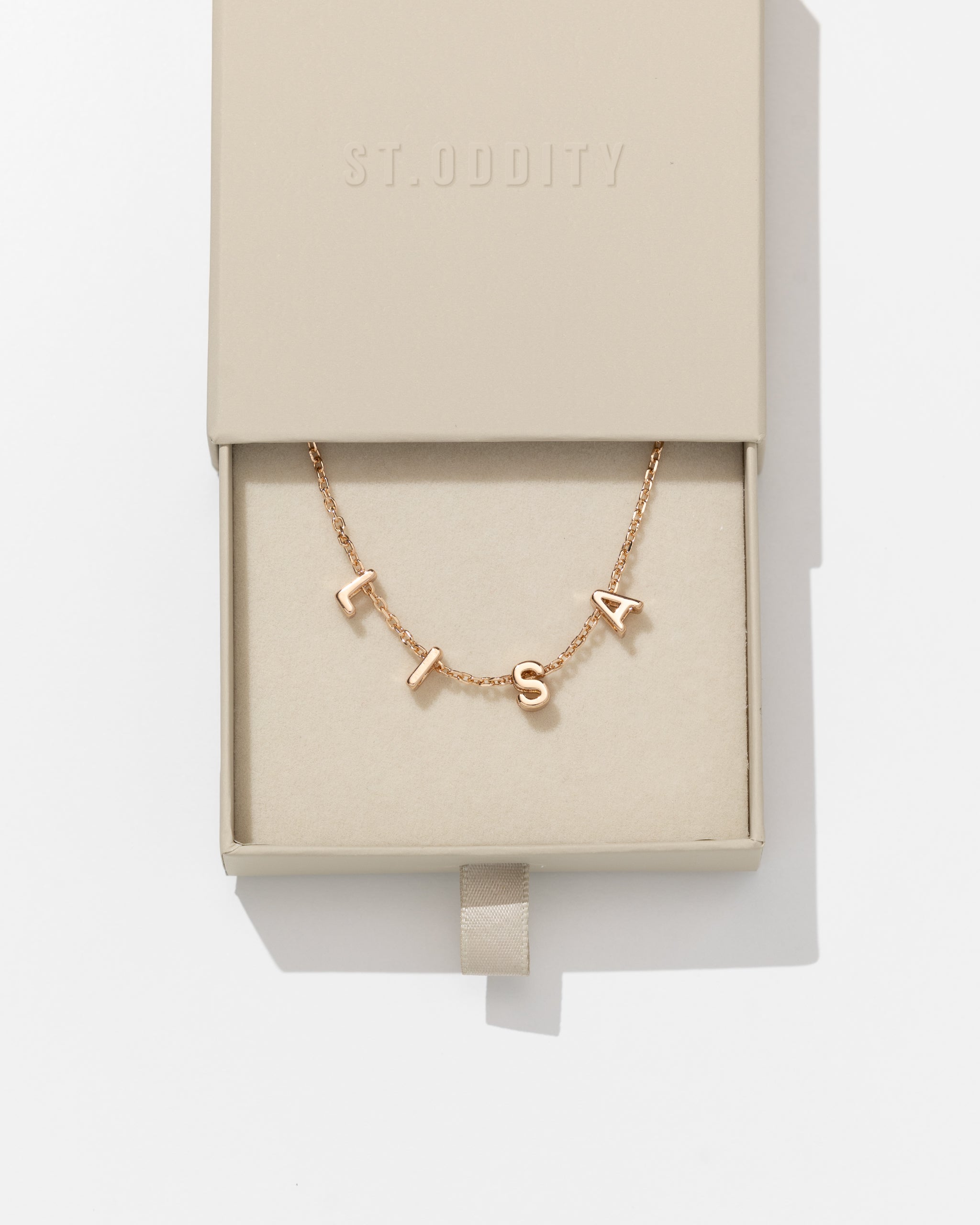Gold fine chain necklace with 'BEC' personalised on it in beige box