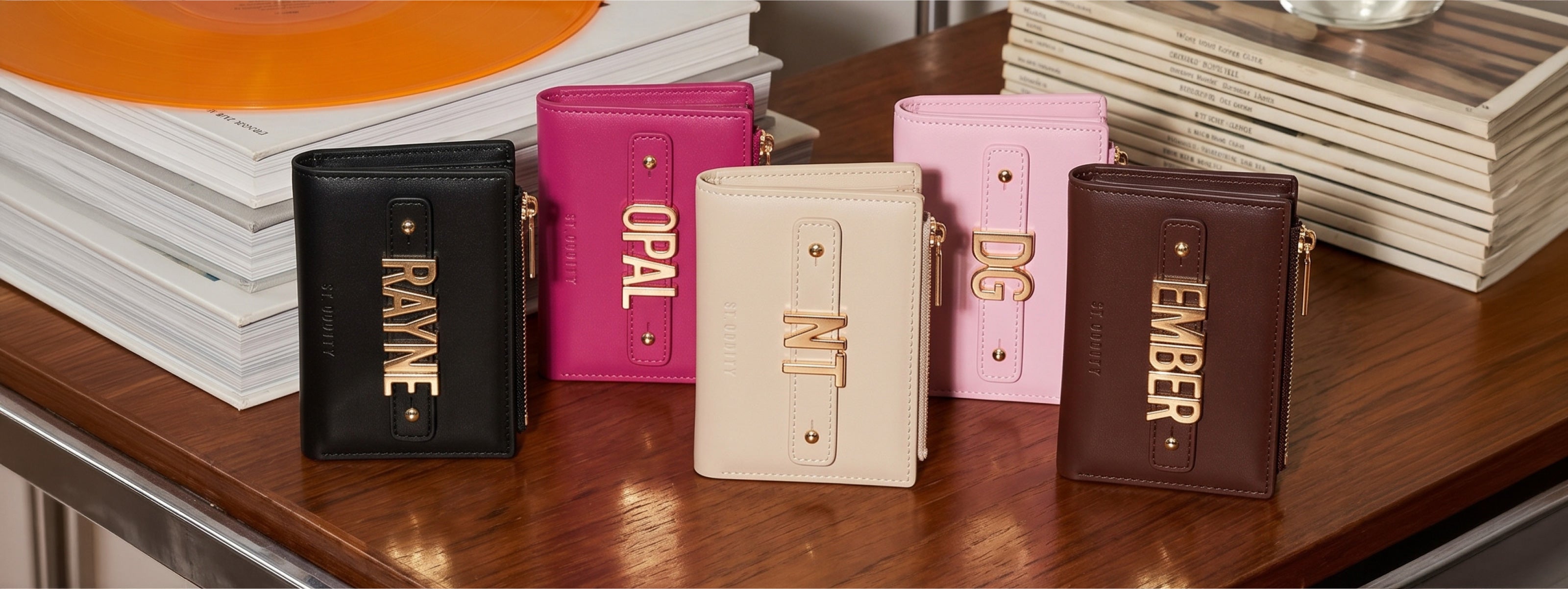 Five small wallets in different colours with personalisation on a wooden surface.