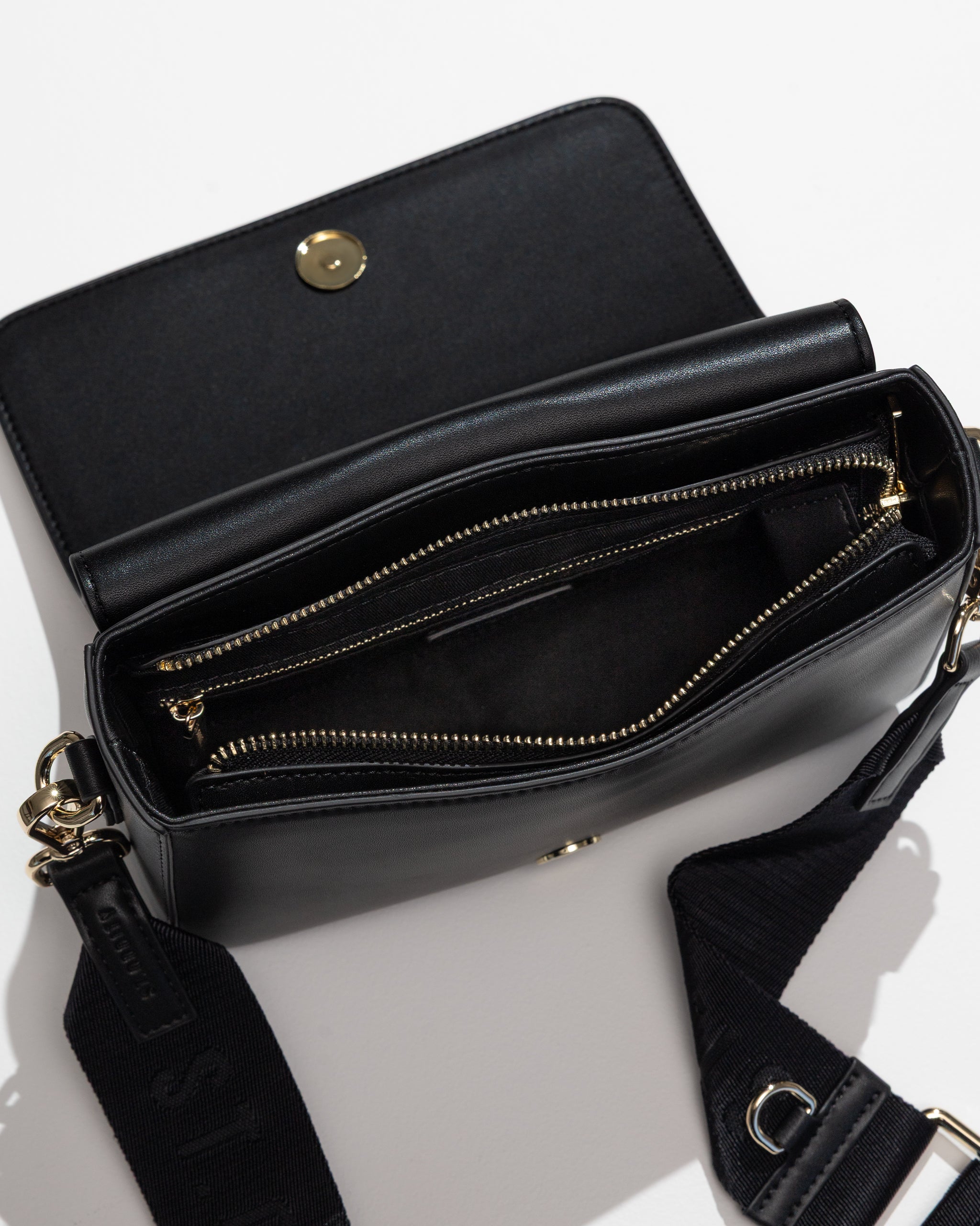 Open black crossbody bag with zip and internal pockets on a white background
