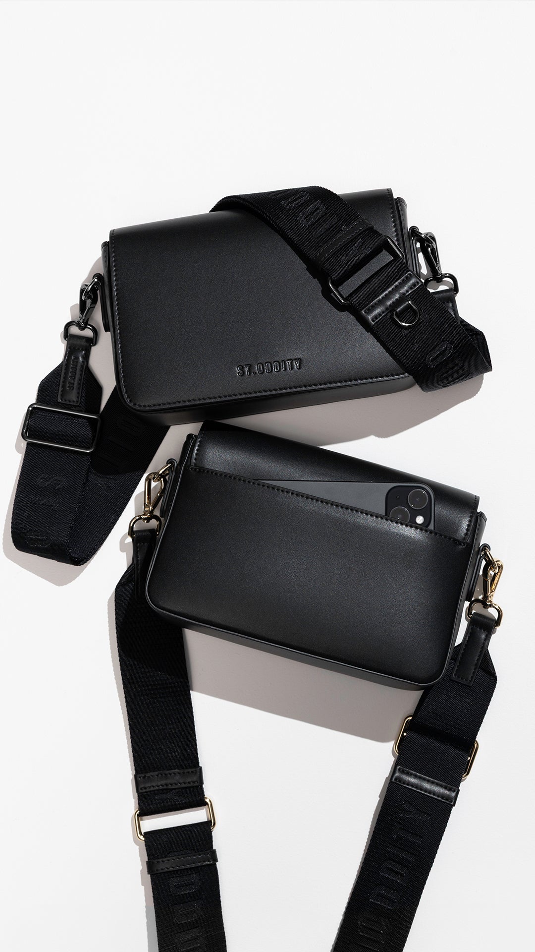 Two black leather crossbody phone bags with adjustable black straps and gold-tone hardware, arranged on a clean white background.