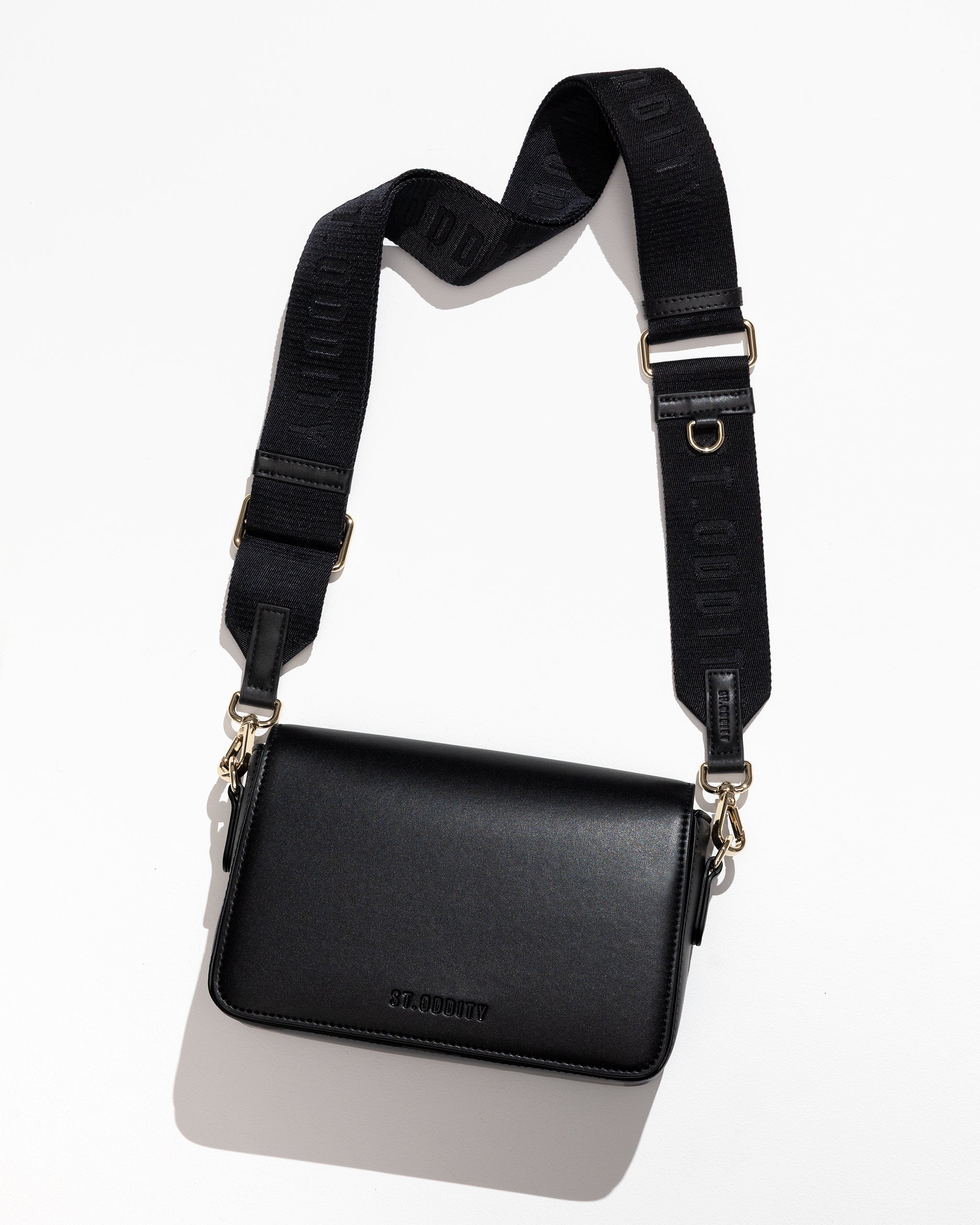 Flatlay of black crossbody bag with adjustable strap on a white background