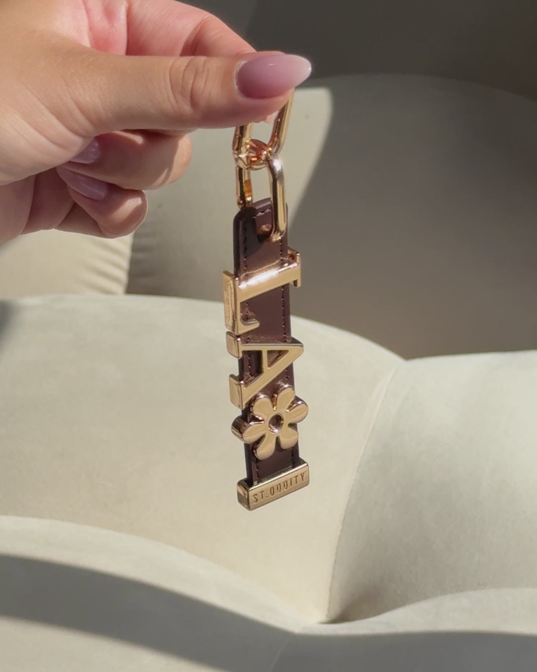 Model holding brown charm with gold personalisation against a white couch