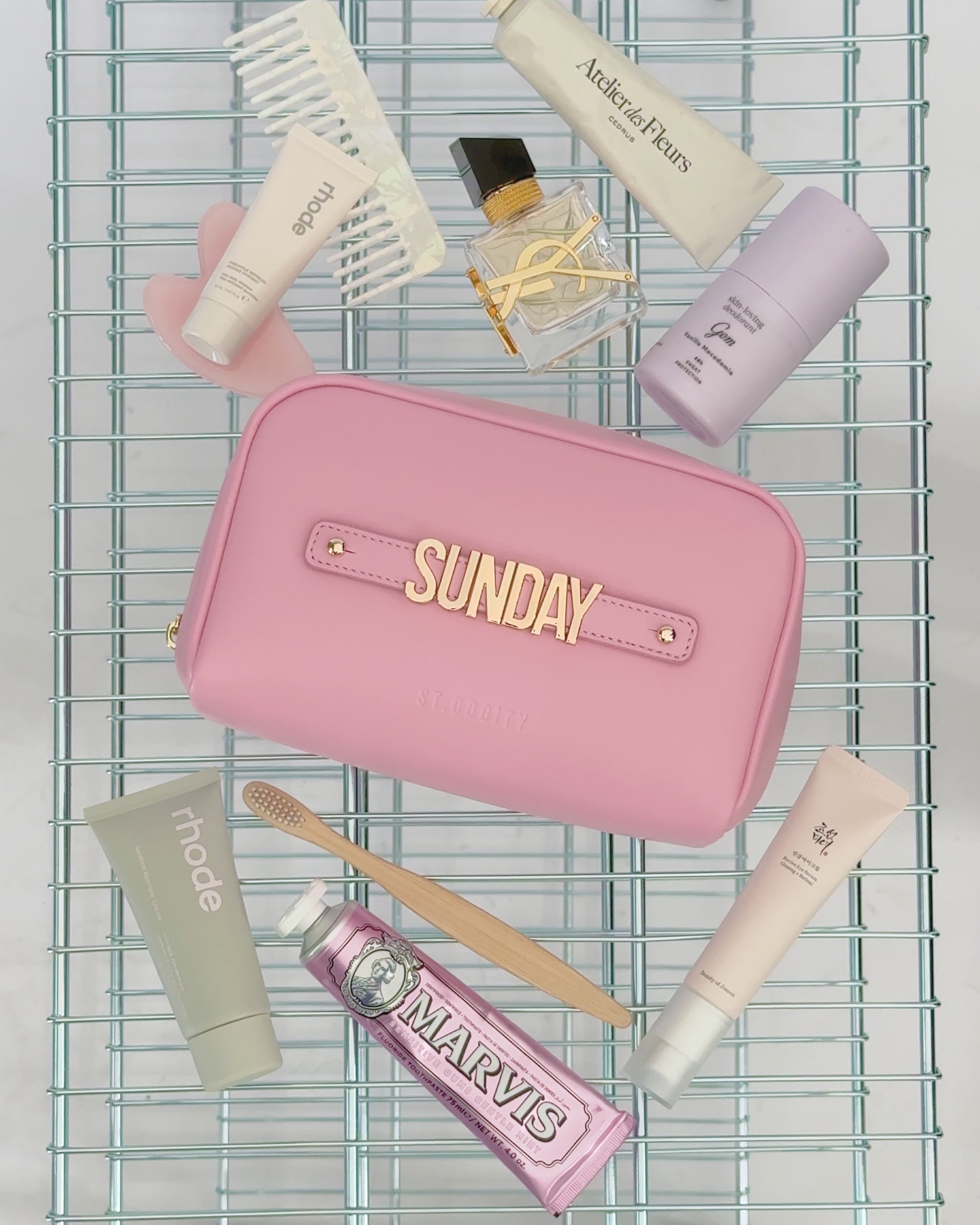 Pink pouch with personalisation 'SUNDAY' and various toiletries on a wire rack
