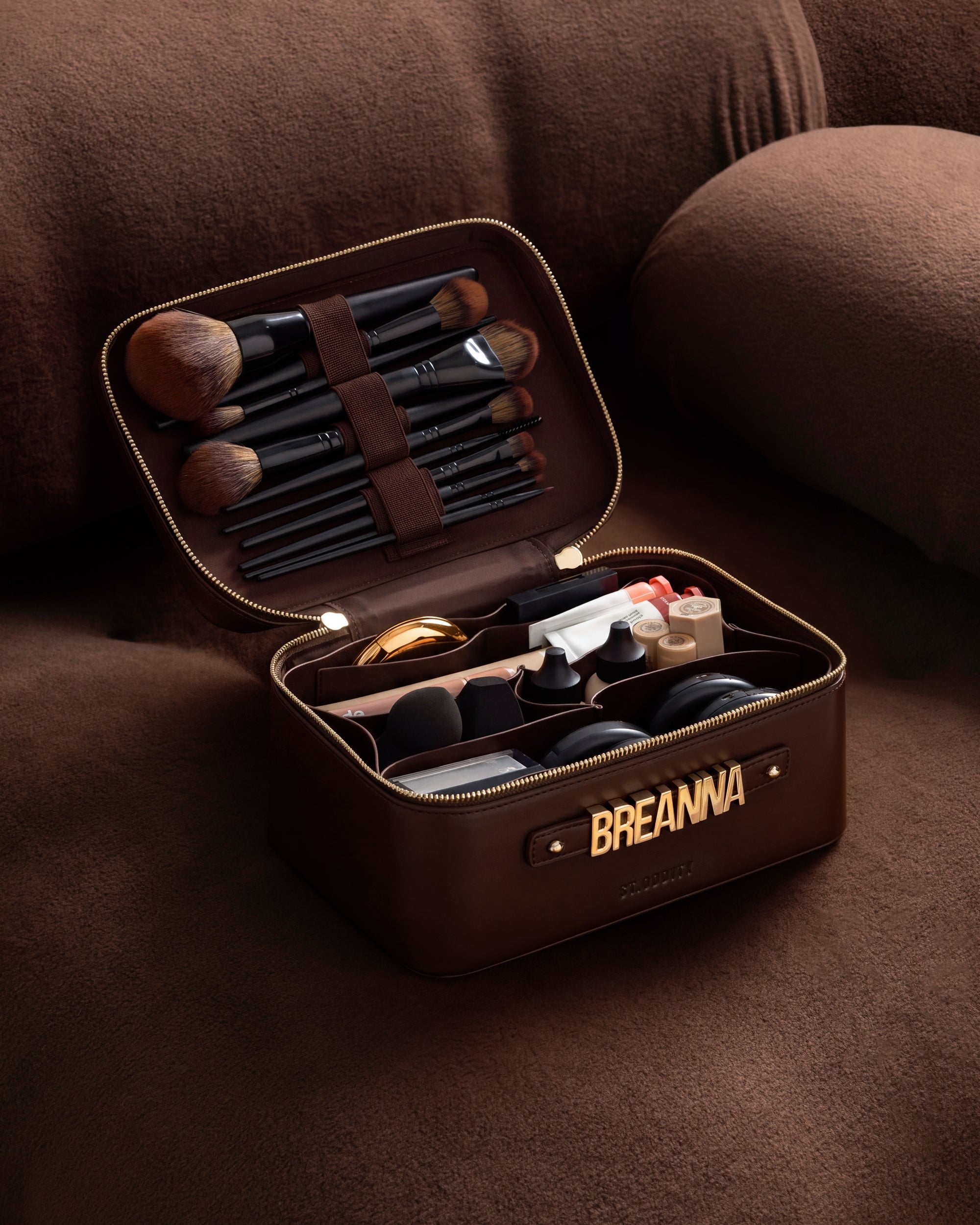 Open brown makeup case with various cosmetic items on a brown couch