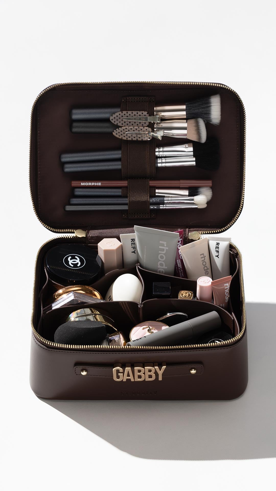 Vanity case in brown filled with cosmetics and makeup brushes.