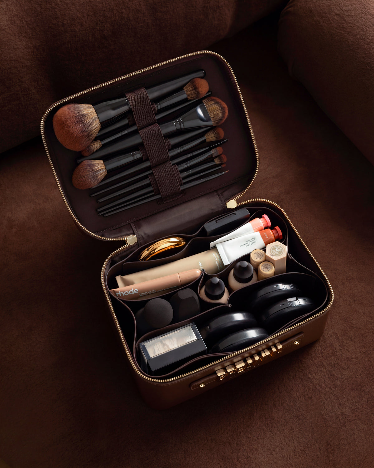 Open brown makeup case with various cosmetic items on a brown couch