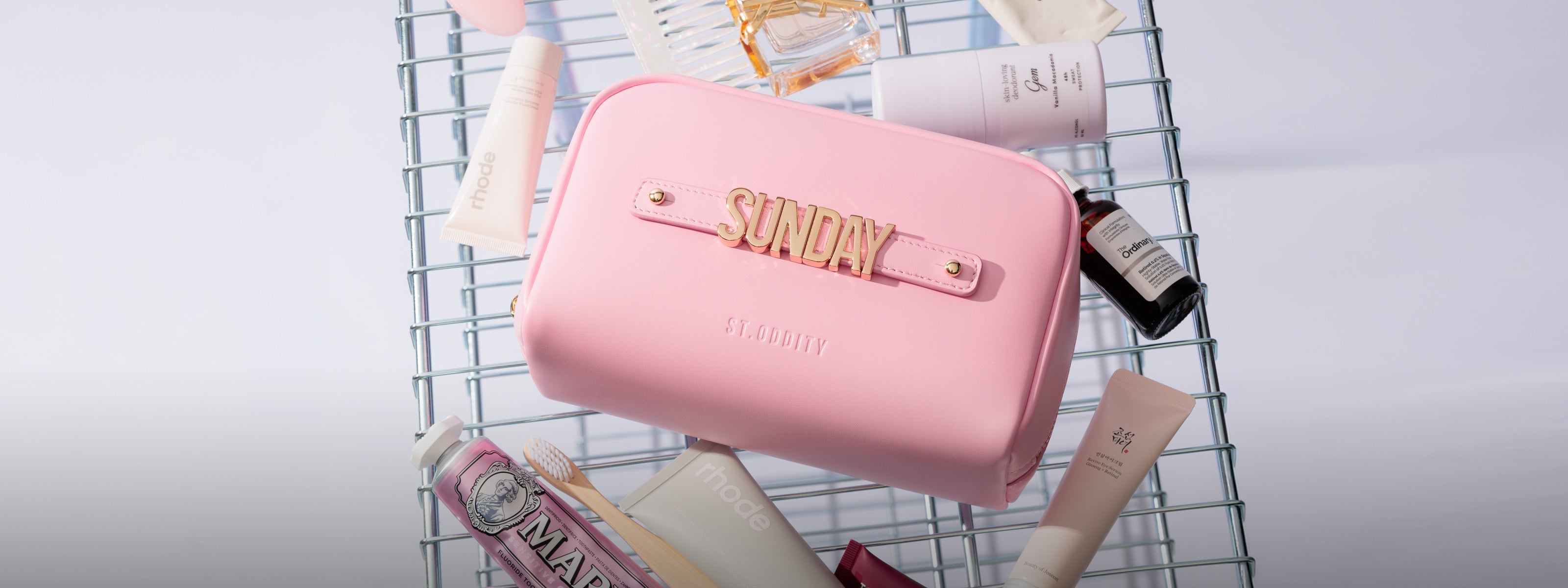 Pink pouch bag with 'SUNDAY' personalisation on a wire rack with beauty products.